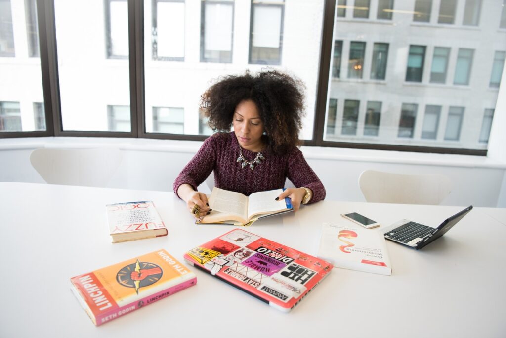 woman reading books at desk with open laptop