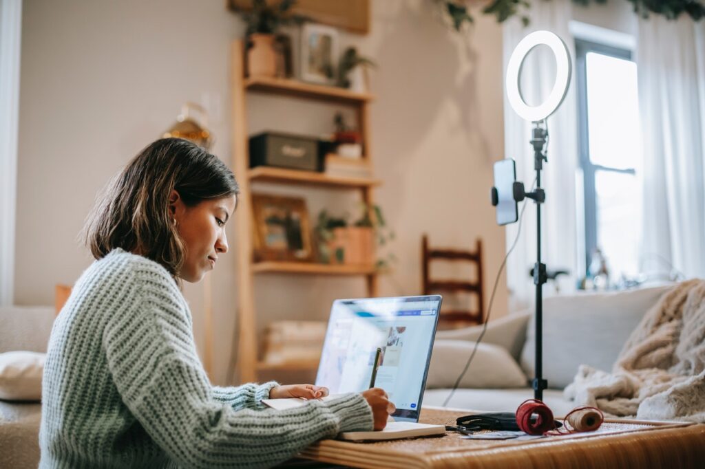 Young woman writing in front of laptop and ring light