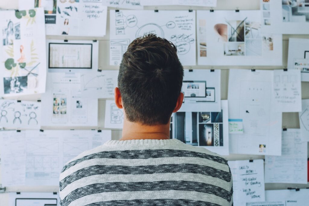 Man standing in front of pin board with multiple ideas on sheets of paper