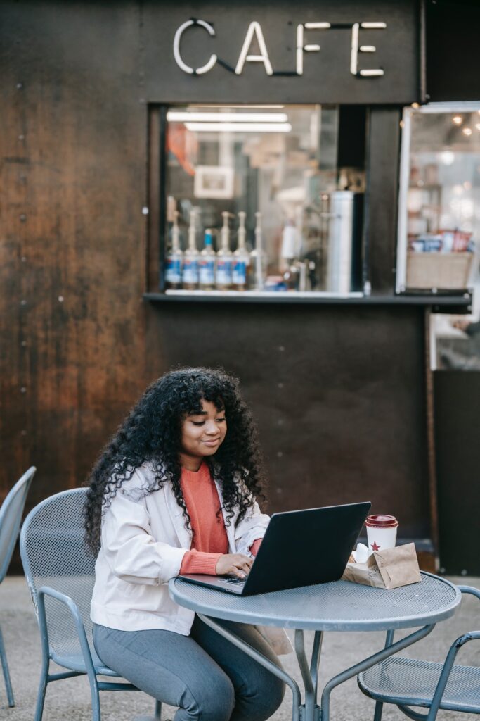 Woman sitting outside cafe typing on laptop