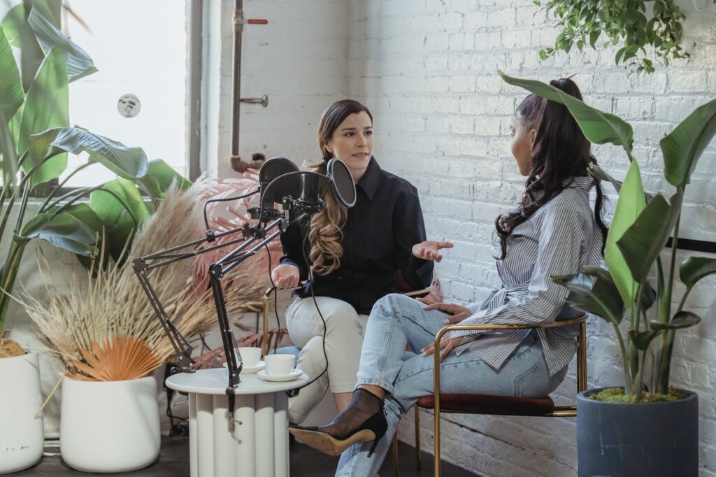 Two women talking in front of microphone for a podcast