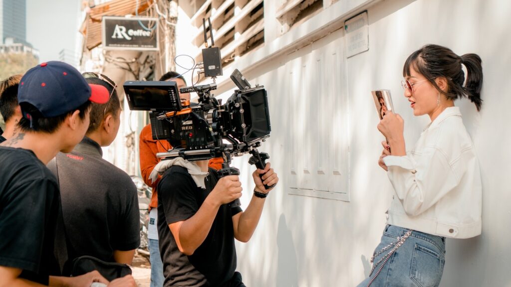 Video camera filming woman standing against a wall with a phone 